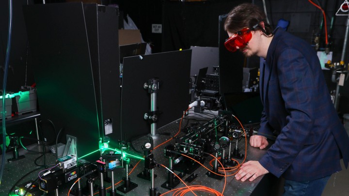 Research graduate student Dustin Roberts wearing goggles and standing in front of a machine